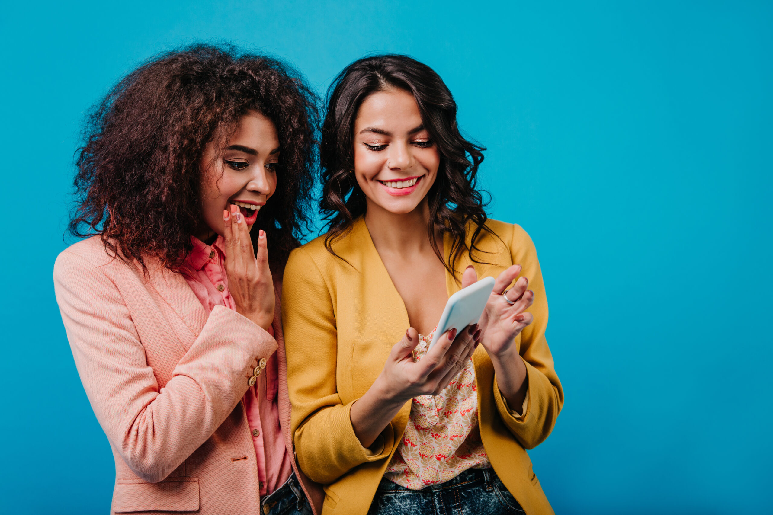 Deux jeunes femmes professionnelles, qui utilise C.A.I.L., ton coach en vente, avec des états de surprise et de joie.