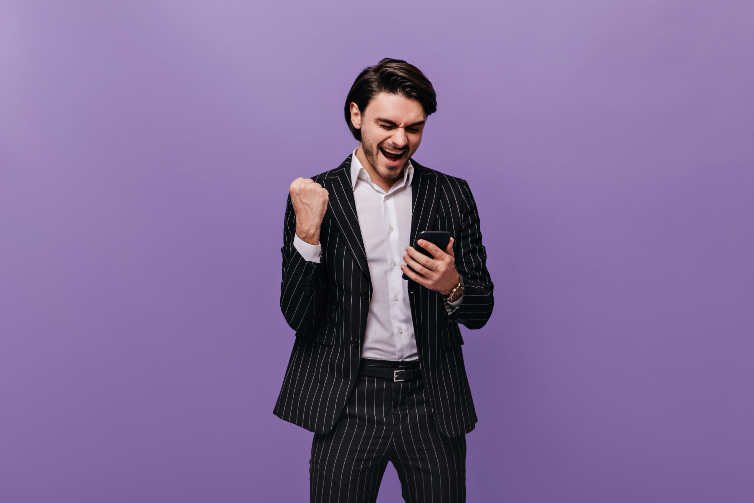 Homme professionnel qui tient son téléphone cellulaire et qui lève le poings, criant sa joie d'avoir conclue une vente grâce à C.A.I.L., ton coach en vente.