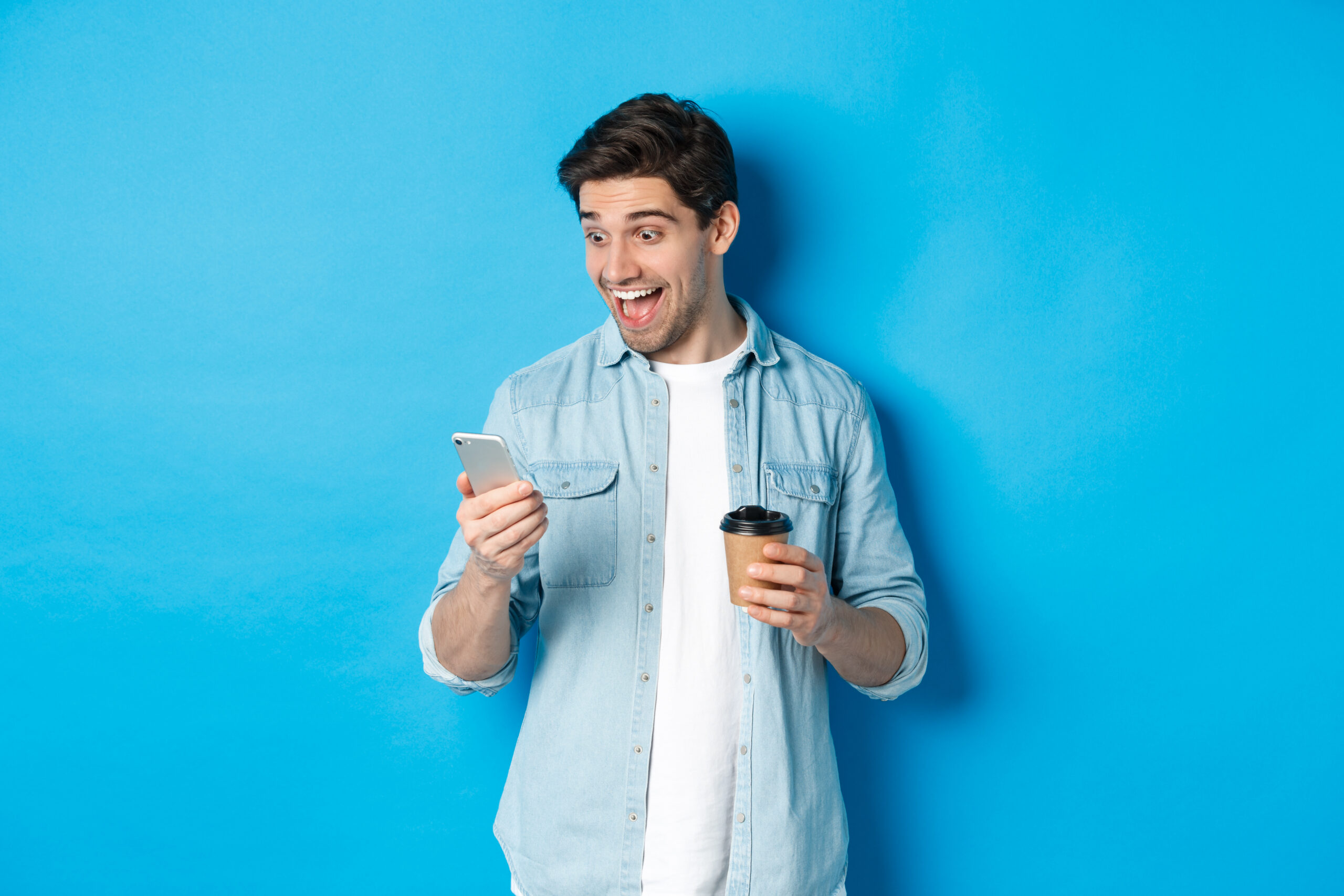 Jeune homme relax, en état de joie et surprise, qui regarde son téléphone cellulaire afin de consulter C.A.I.L., ton coach en vente.